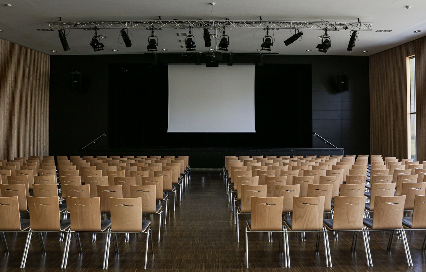 Empty modern conference hall with wooden chairs facing a stage.