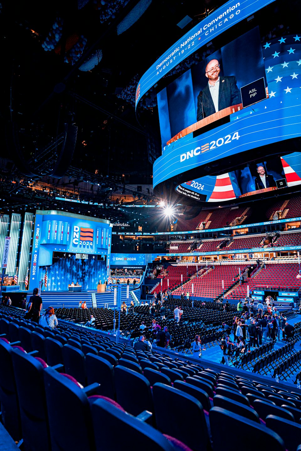 People move through rows of empty seats at a political convention.