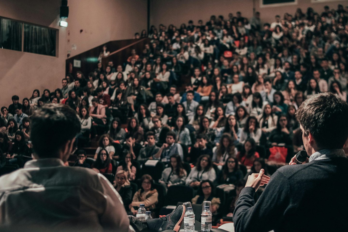 Speakers on stage presenting to a large audience in an auditorium.